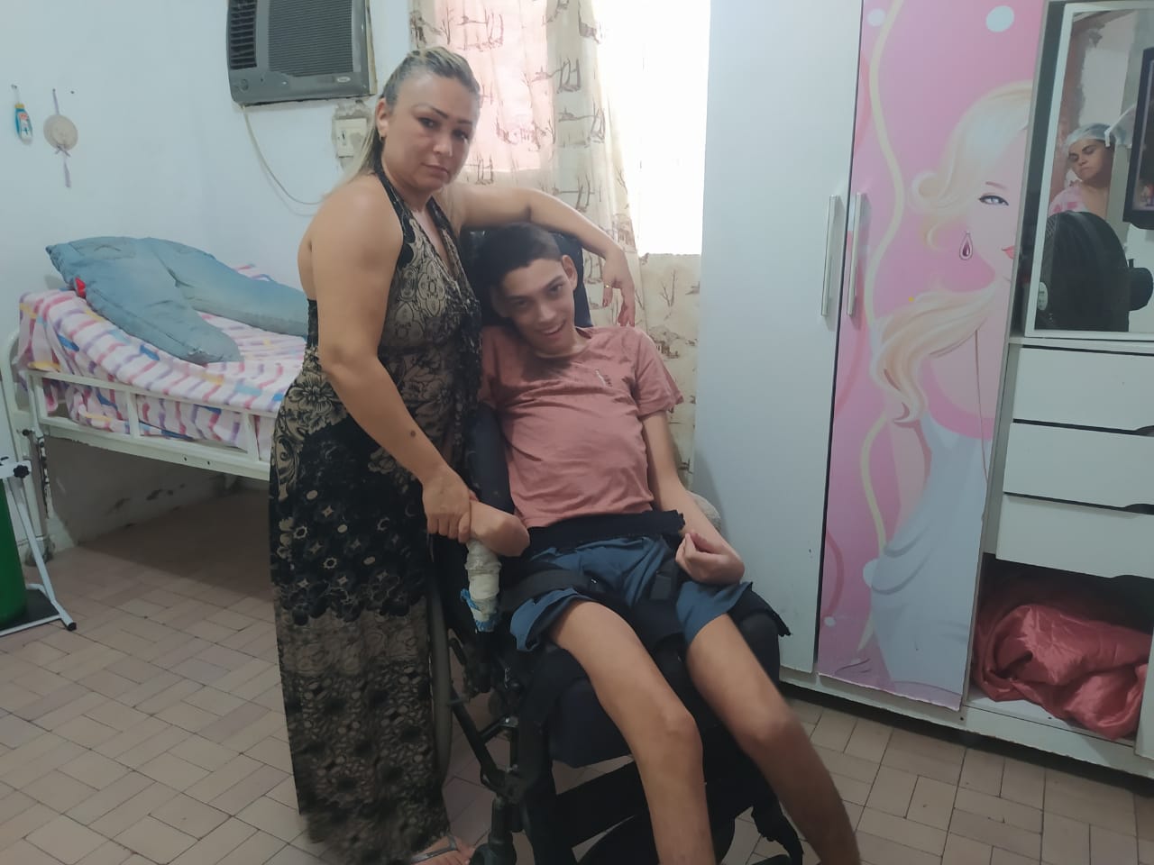 Gilmara Costa ao lado de seu filho com a nova cadeira doada por Rejane Dias