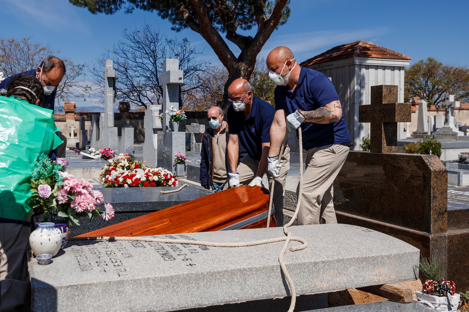 Funcionários de uma funerária usam máscaras durante o enterro de vítima da COVID-19 no cemitério de Fuencarral em Madri, na Espanha