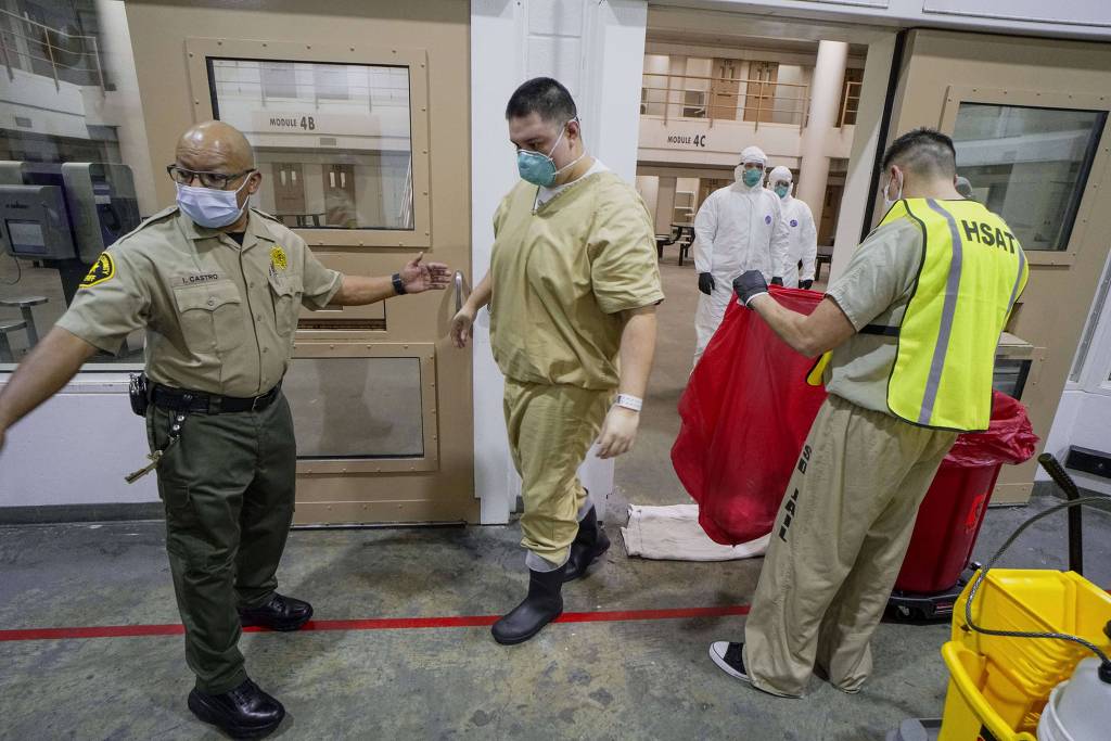 Presos tiram seus equipamentos de proteção depois de limpar uma cela para impedir a propagação do coronavírus em uma cadeia de San Diego, nos EUA