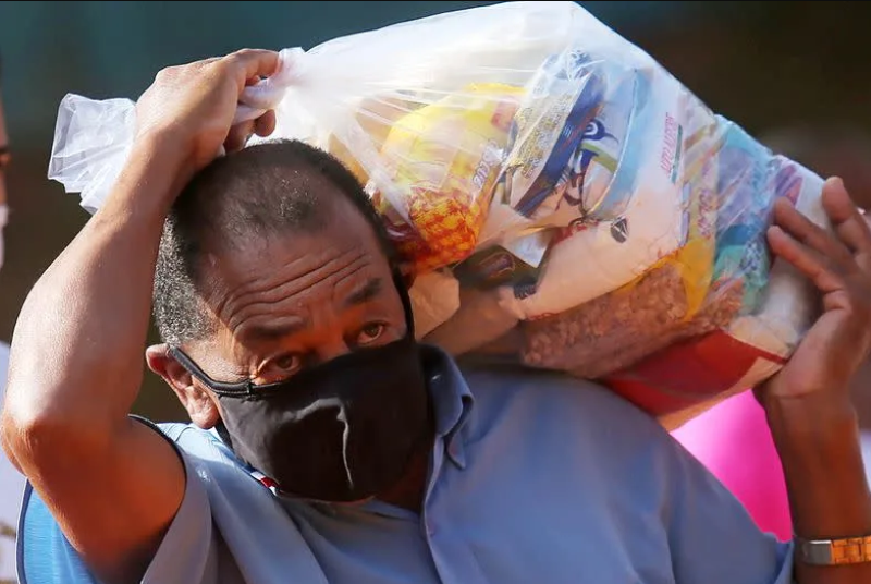 Morador de rua em SP carrega cesta básica distribuída durante a pandemia da COVID-19