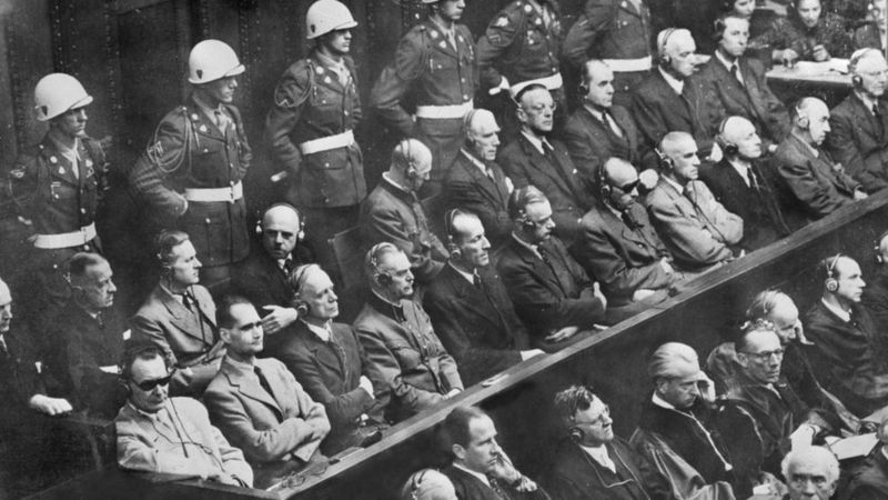 No canto inferior esquerdo, usando óculos escuros, está Hermann Göring, seguido por Rudolf Hess, os réus mais notórios