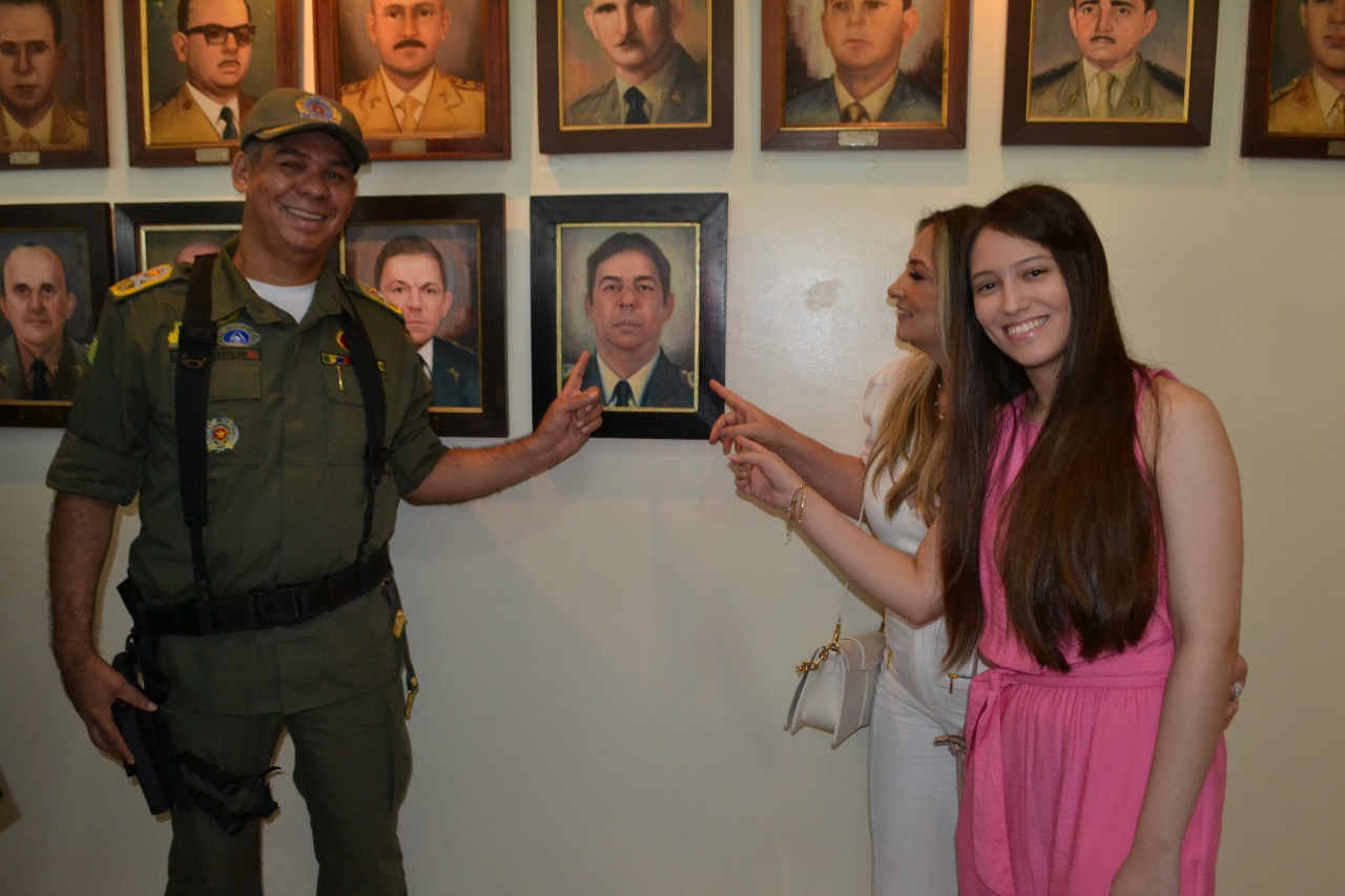 Coronel Lindomar, sua esposa Sra. Cruz e sua filha Carol posam ao lado da foto do ex-comendante