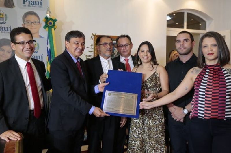 Wellington Dias e o então diretor da ACADEPEN/PI, Jacinto Teles entregam placa a Karine Barros, Rebeca Filha e Bruno Maia, em homenagem aos primeiros concludentes do CFI-2018
