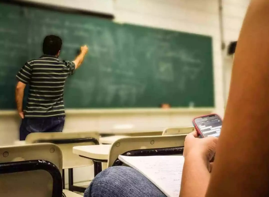 Jovem com celular na sala de aula